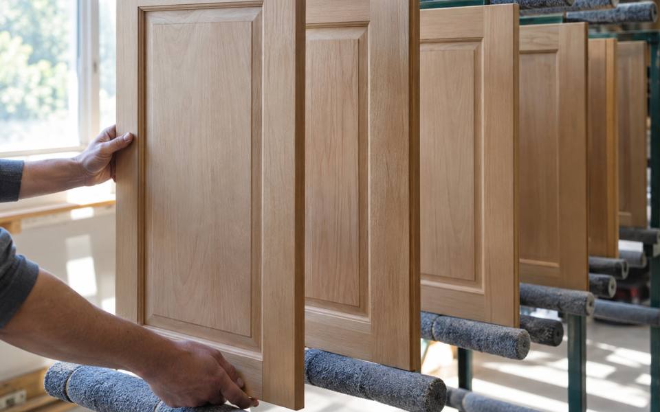 A bare wood cabinet door being wiped down and prepared for its first coat.
